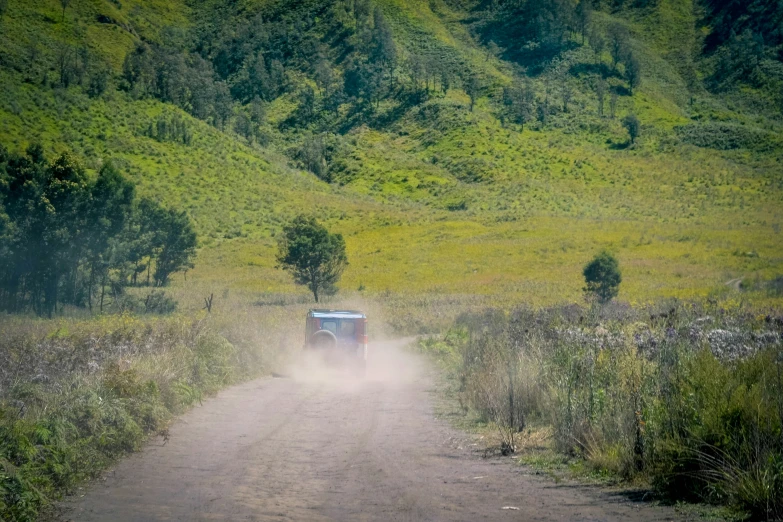 truck traveling down dirt road past hills and trees