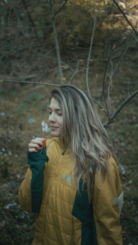 a woman in yellow jacket looking at flower in forest
