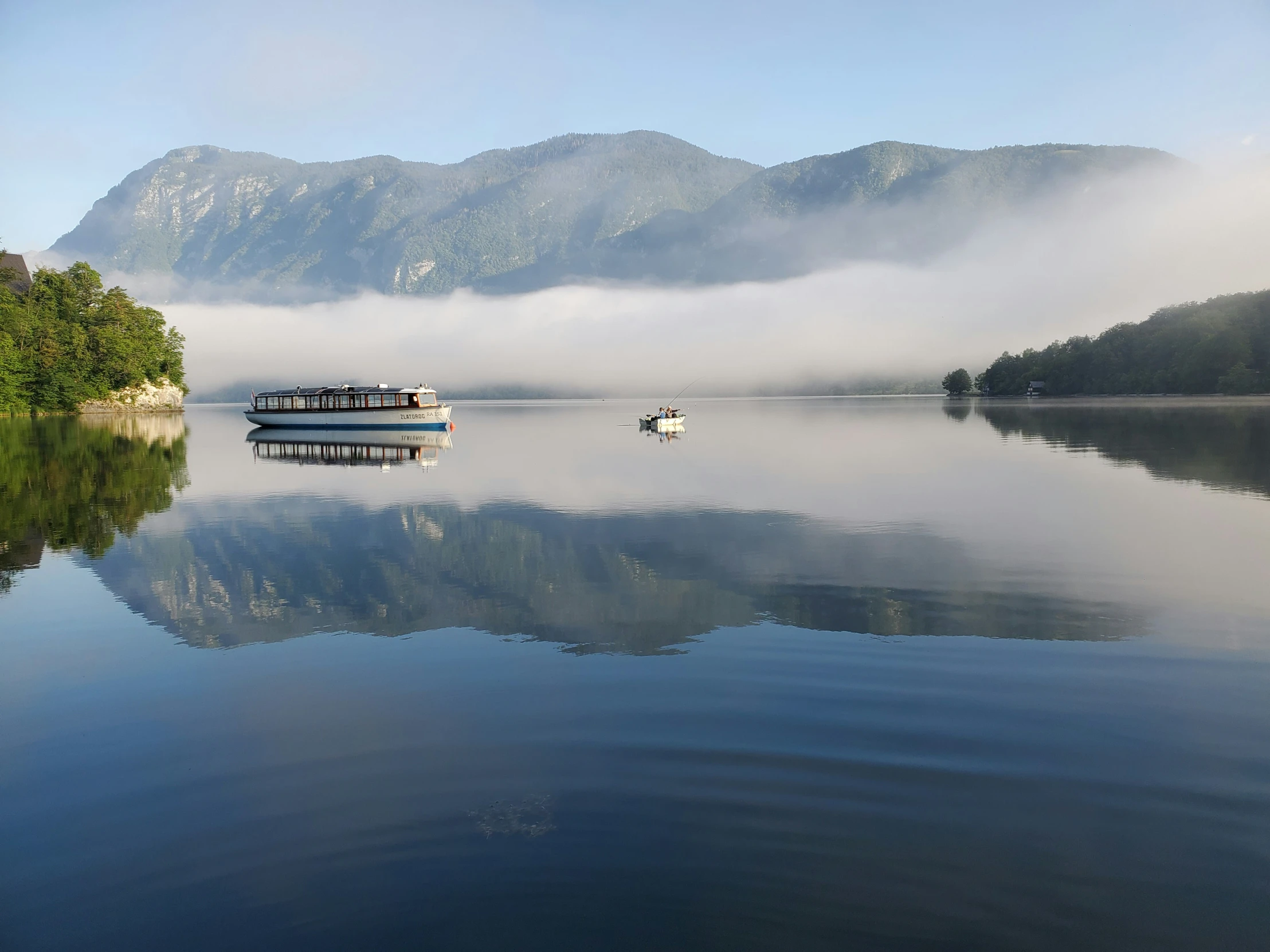 a ferry boat on a still lake surrounded by fog