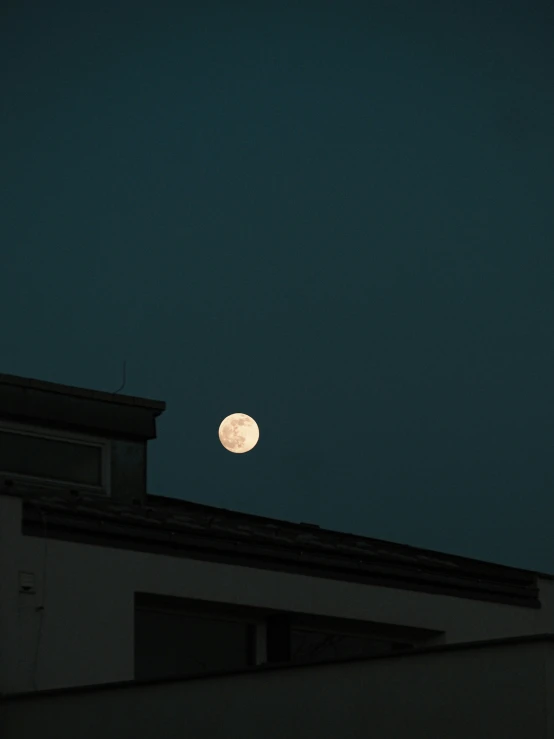 the full moon seen over a roof and window