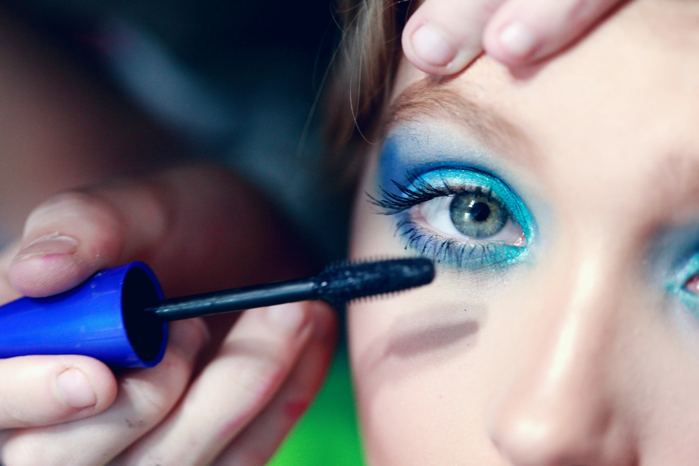 woman with blue and green eyes painting her lashes