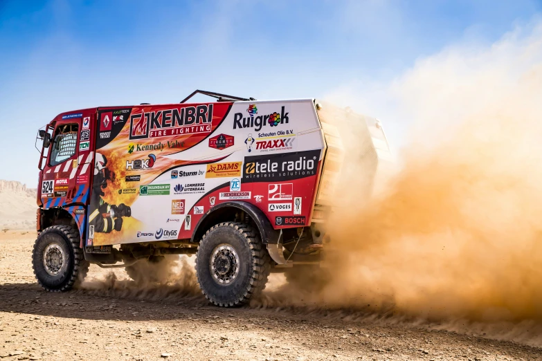 a truck drives on dirt as dust pours around it