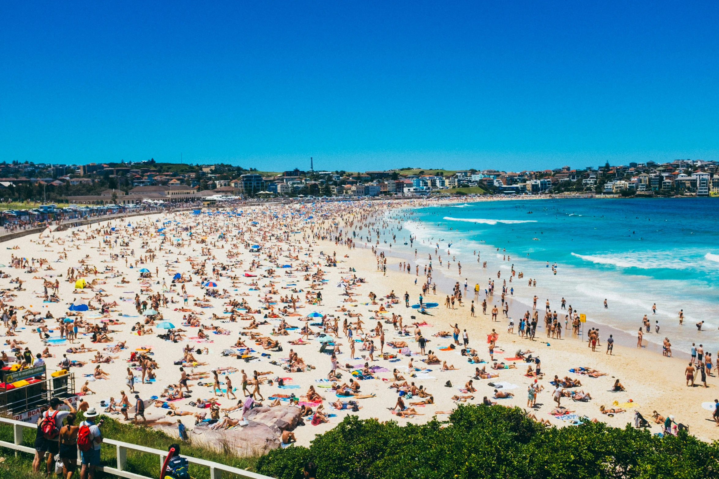 a crowded beach next to a blue ocean with people on it