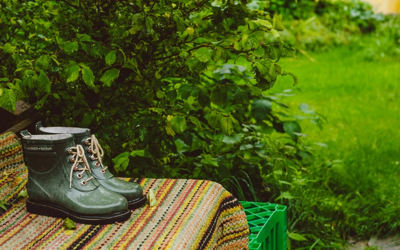 someone wearing black boots is sitting on a blanket by a tree