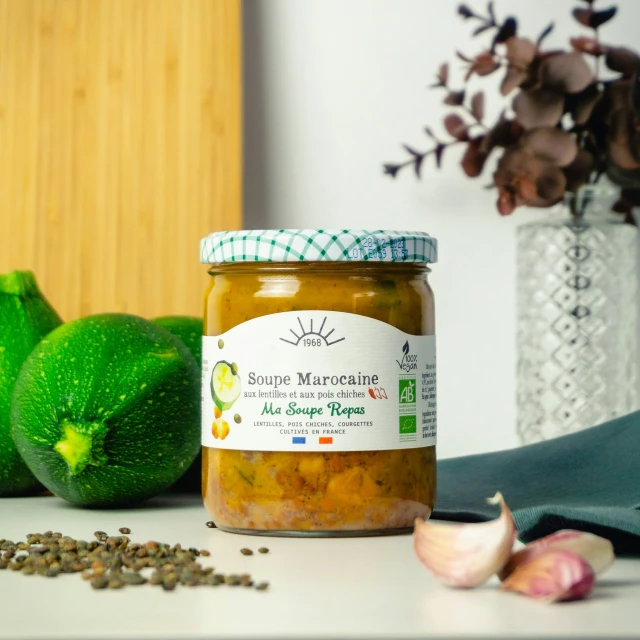 a jar of soup sits next to some vegetables