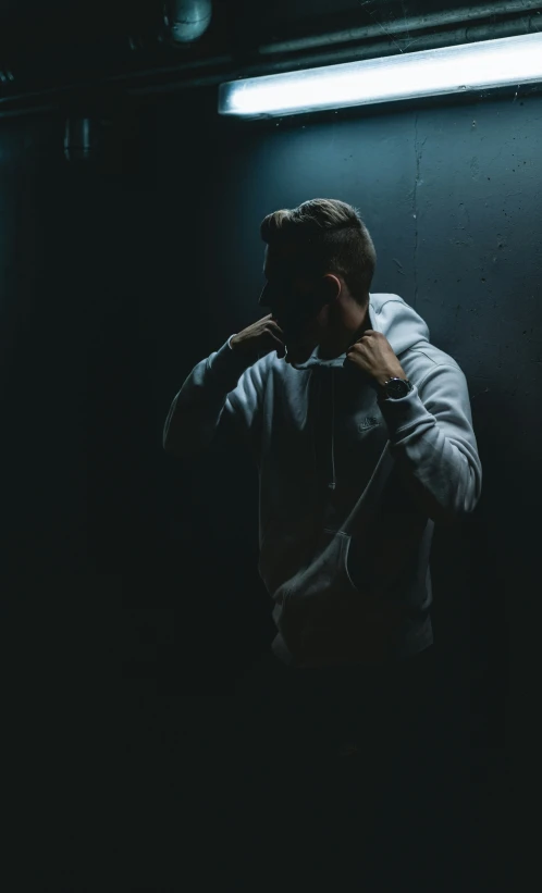 a man standing in the dark adjusting his hoodie