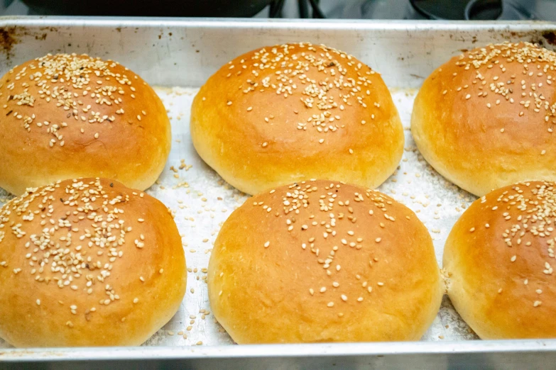 six sesame buns with sesame seed sprinkled on top in a tray