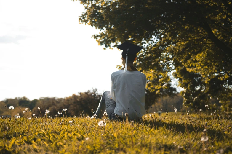 a woman sitting in the grass next to trees on a sunny day