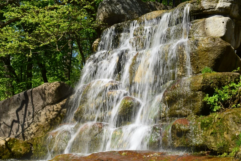 a waterfall is pictured in the forest near rocks