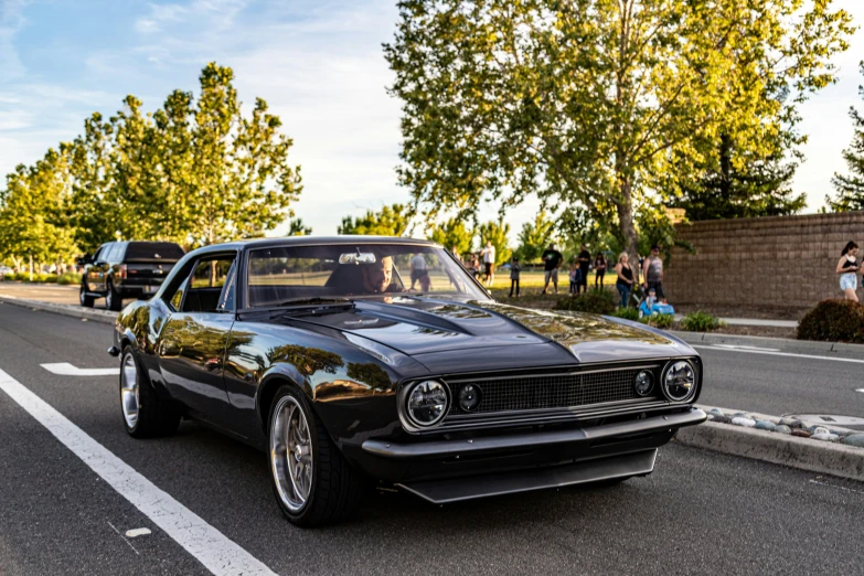 a vintage black muscle car sitting in the middle of a street