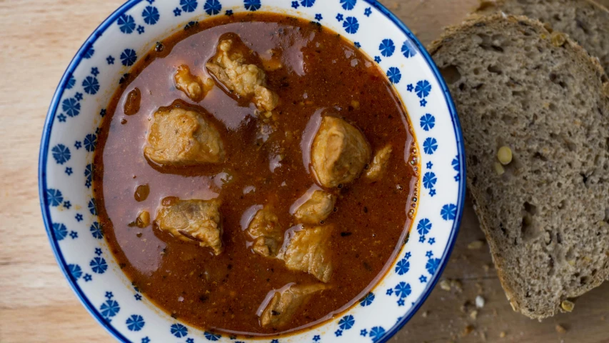 a bowl with some meat in sauce next to bread