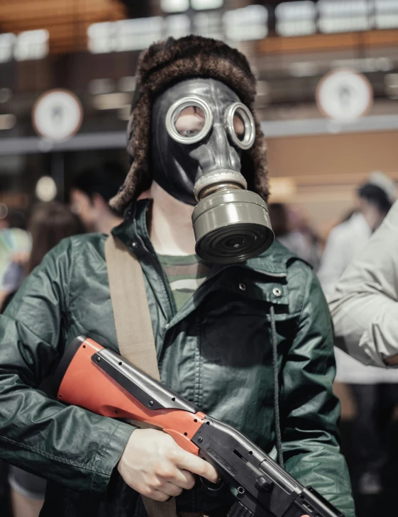 man wearing gas mask and holding a gun and pointing at camera