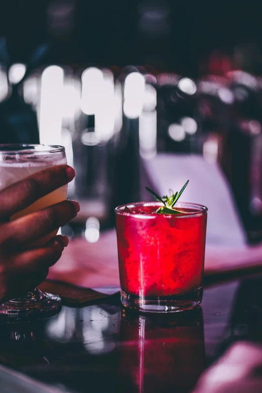 a person holding onto a wine glass next to another alcoholic drink