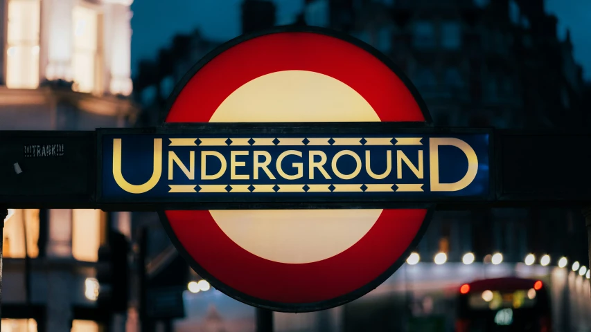 underground sign at night in the city with city lights behind it