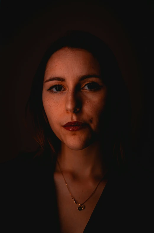 a woman in a dark room looking down with her hand on her chin