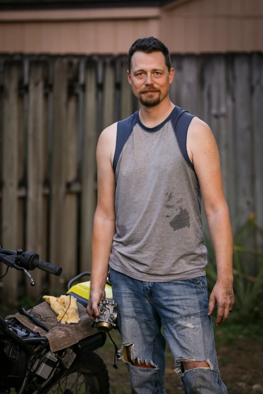 a man posing next to a motorcycle in his backyard