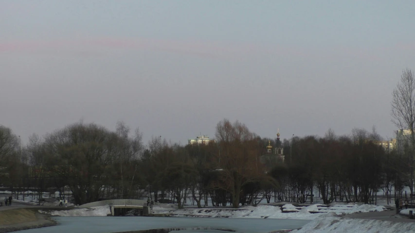 a large tower sits in the background as snow and trees stand near the river