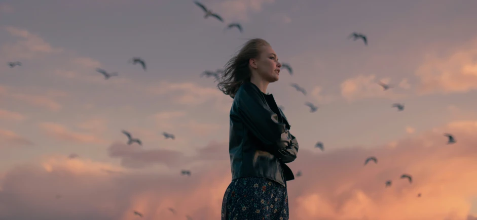 a woman wearing leather standing on the beach watching the birds in the sky