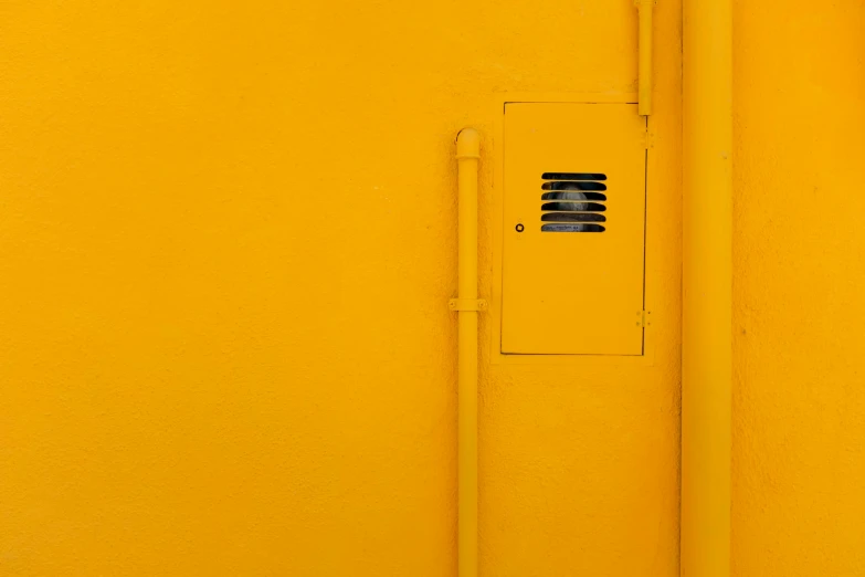 an orange wall with a square air vent and round hole in the corner