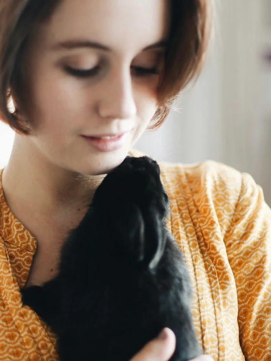 a woman pets a small black cat's ear