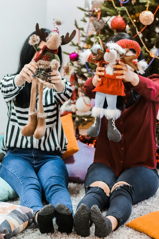 two girls sitting in front of a christmas tree holding stuffed animals