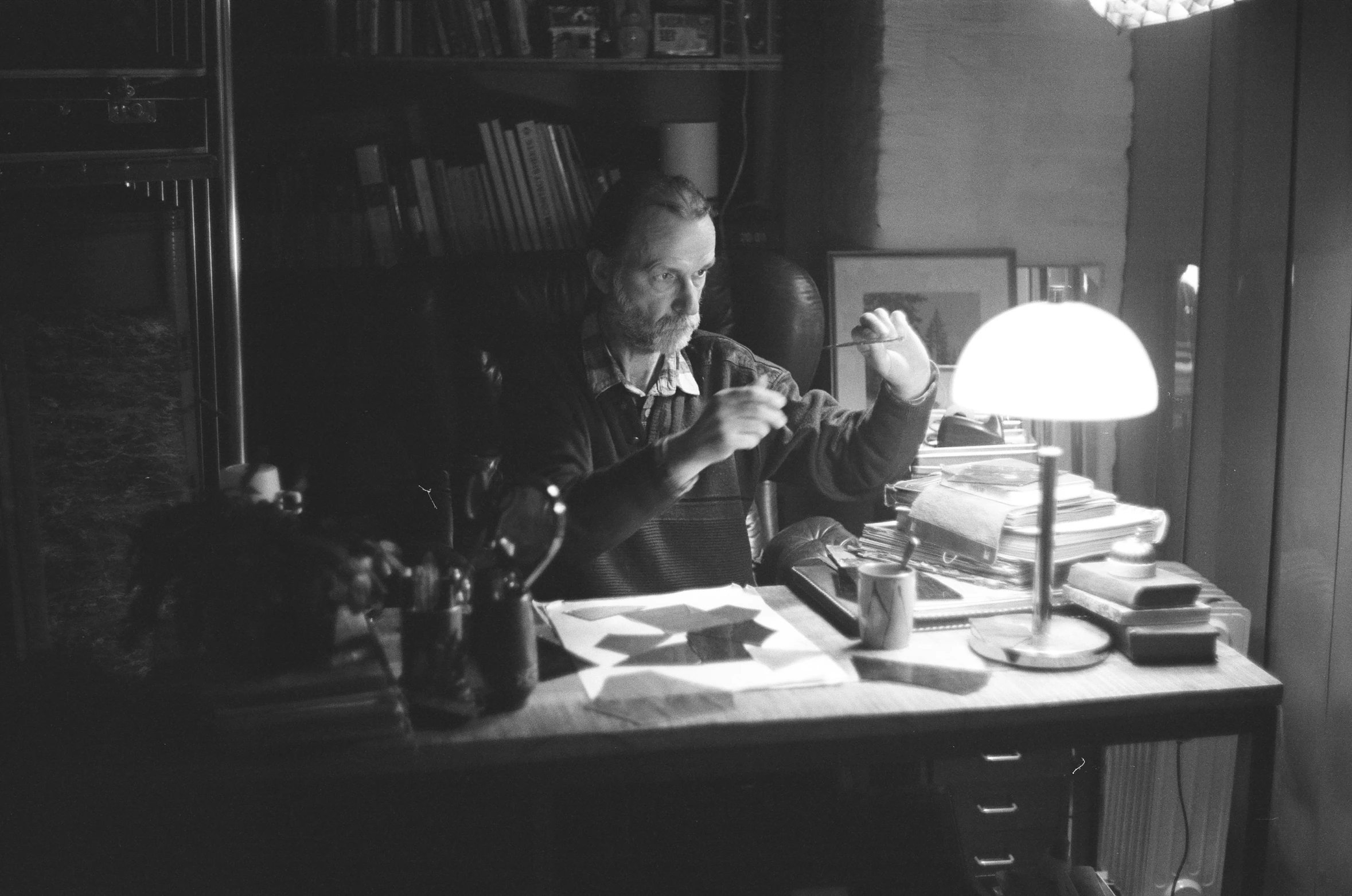 black and white image of man sitting at desk holding scissors