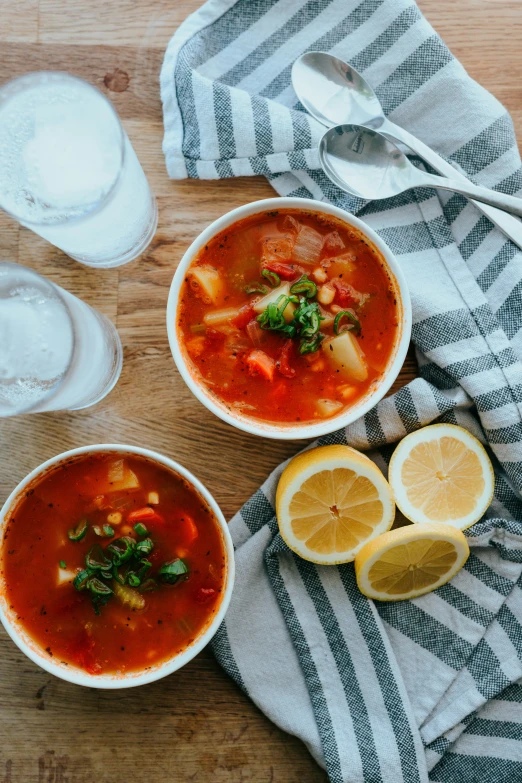 three bowls filled with a creamy soup next to lemon slices and water