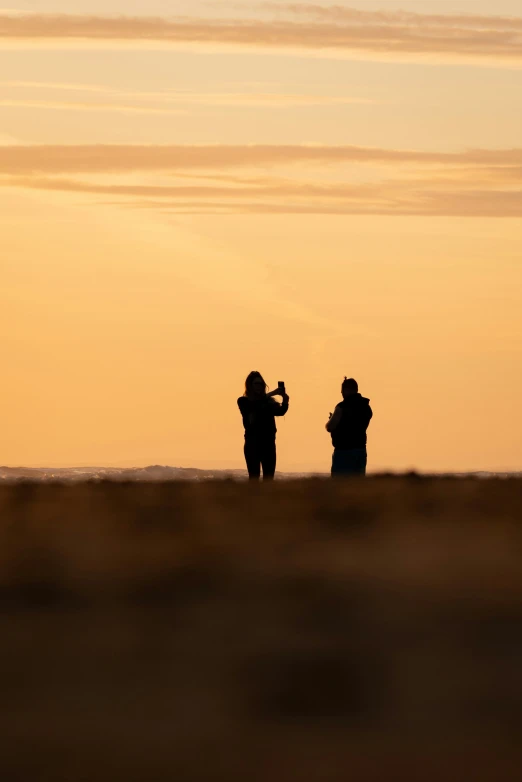 two people flying a kite at sunset near the ocean