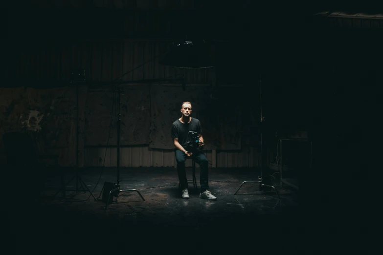 a man is standing in the dark, on the stage with a guitar