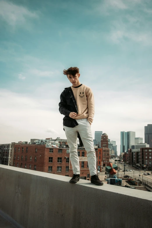 a guy in sweater and jeans stands on a ledge looking at his phone