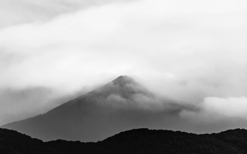 a black and white image of a mountain in the fog