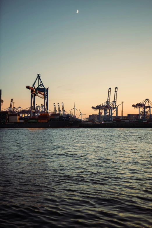 the ship docked at the harbor has many cranes in the distance