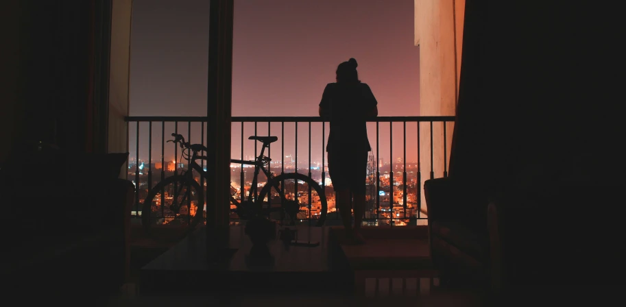 silhouette of a man with a bicycle standing by the balcony