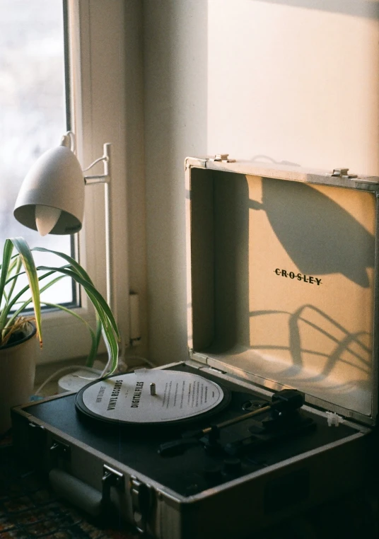 an old record player sitting on top of a suitcase next to a window