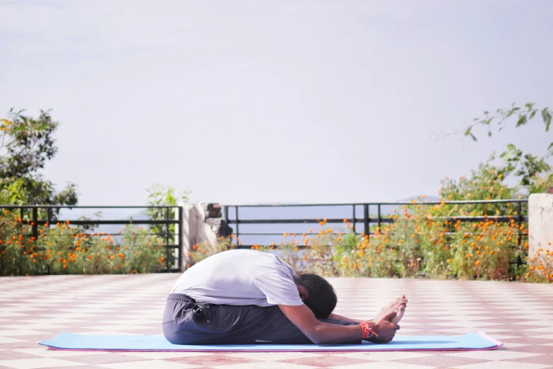 a man in white shirt doing yoga outdoors on blue mat