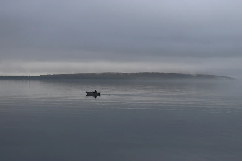 a small boat sits in calm water as fog looms over a shore