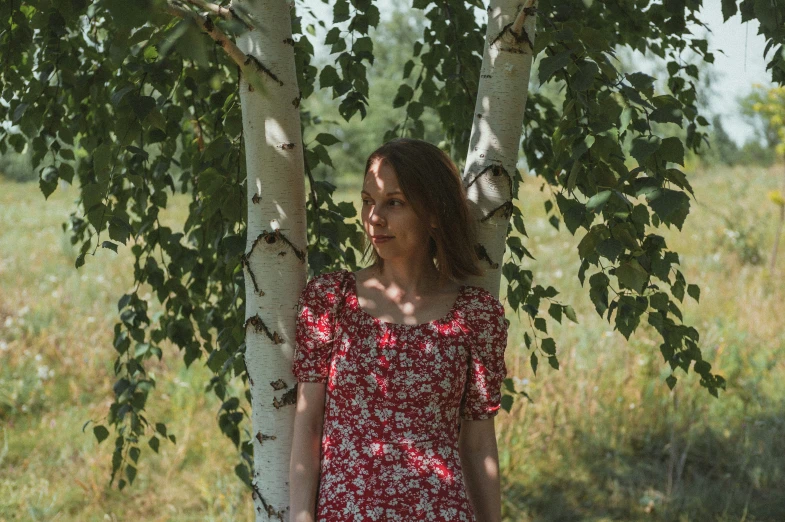 a woman in a red floral dress standing behind a tree