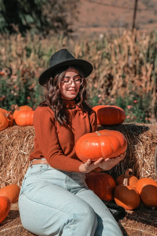 a  sitting in front of hay filled with pumpkins