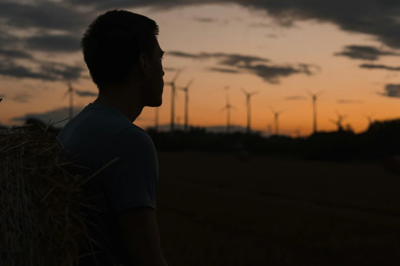 a man with hay on his back and wind mills in the background