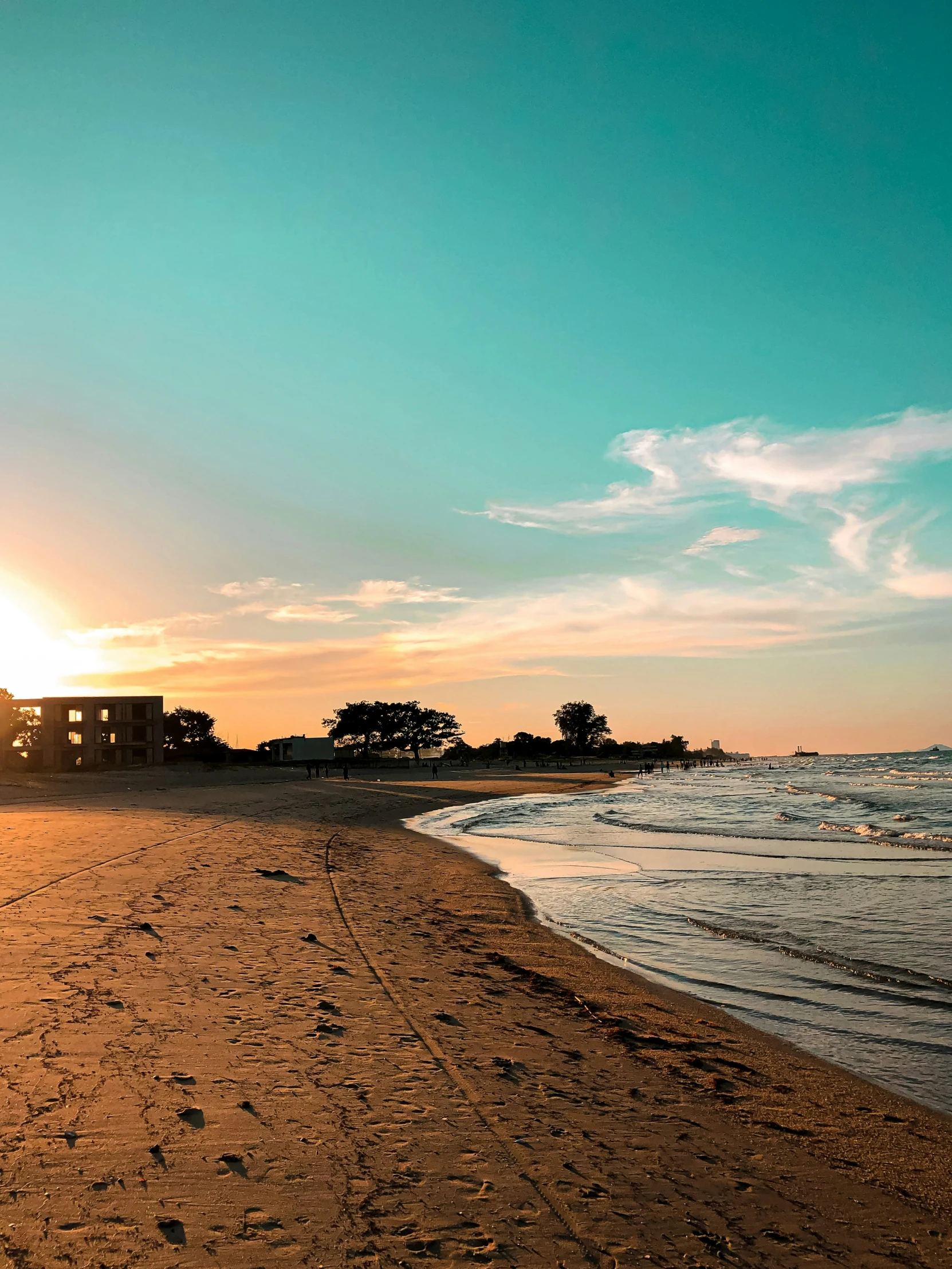 a beach area at sunset with a building on the horizon