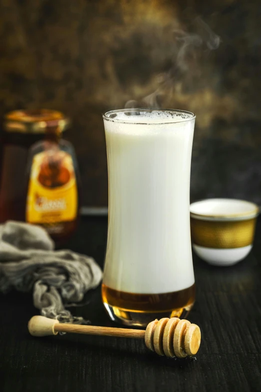 a glass on a table with honey and a spoon