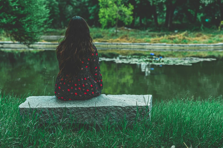 the girl is sitting on a stone block near water
