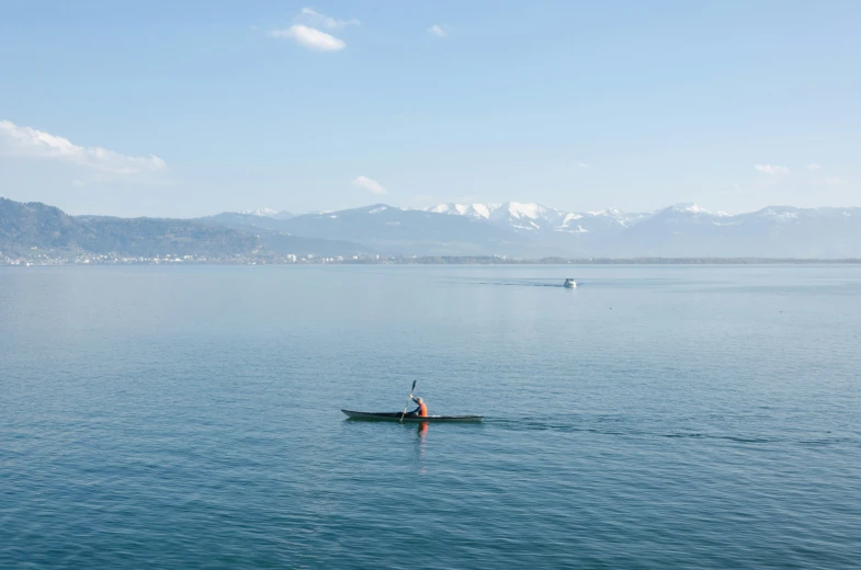 a lone person paddles on the still waters