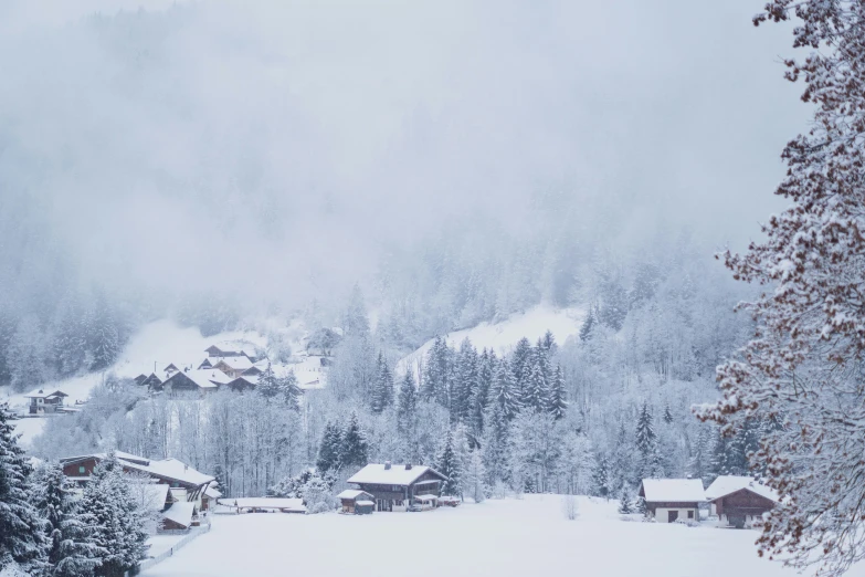 a snowy day in a village with the mountains covered in clouds