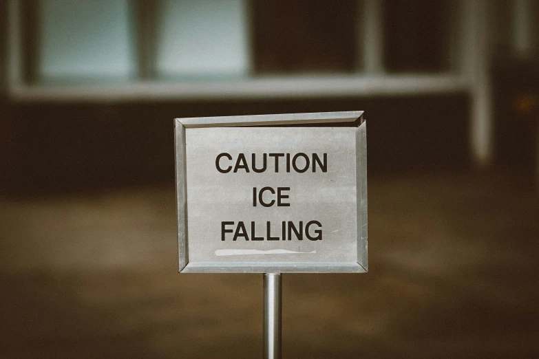 a white sign saying caution ice falling sitting in front of a building