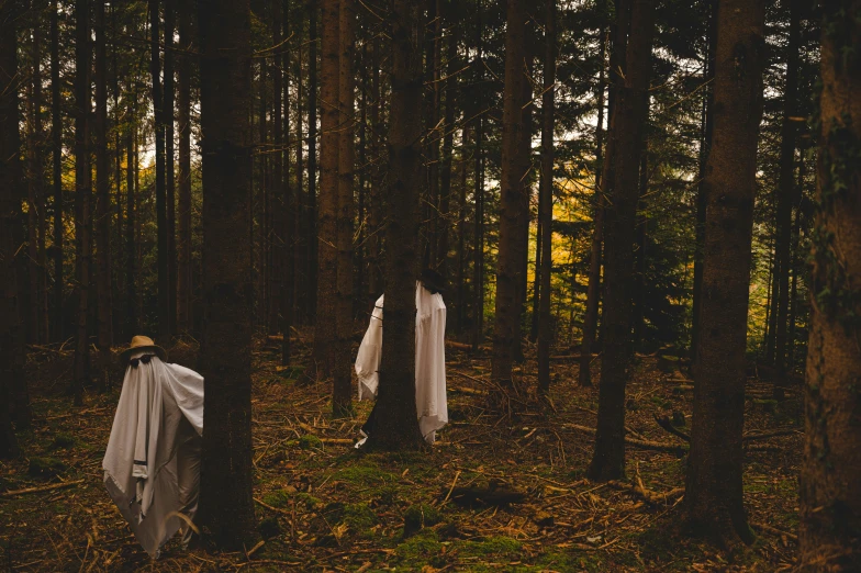 two men in white robes and hats standing in the woods