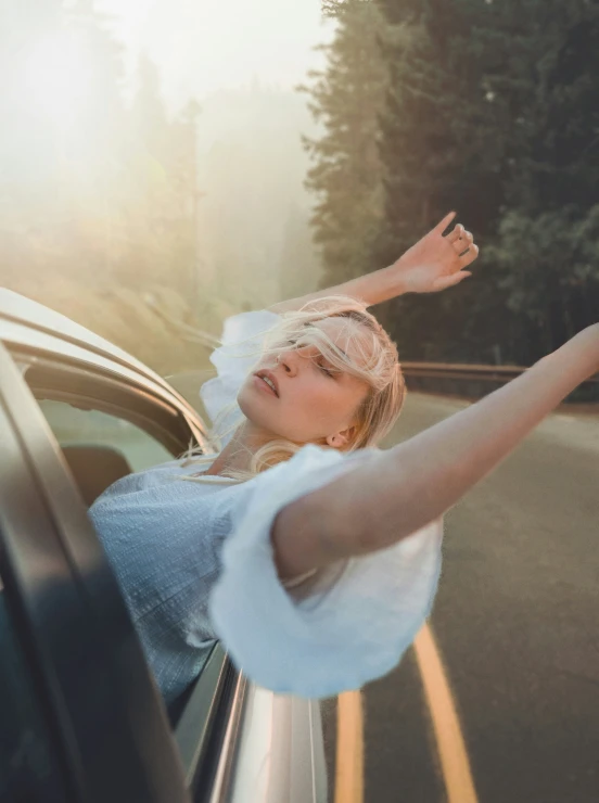 a woman waving from her car window, in front of trees
