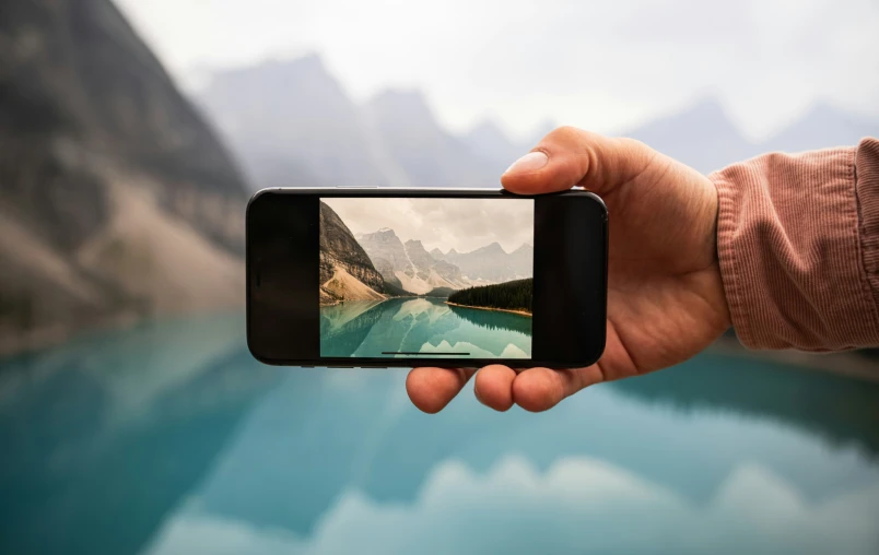 someone holds a cell phone to take a po of mountains and water