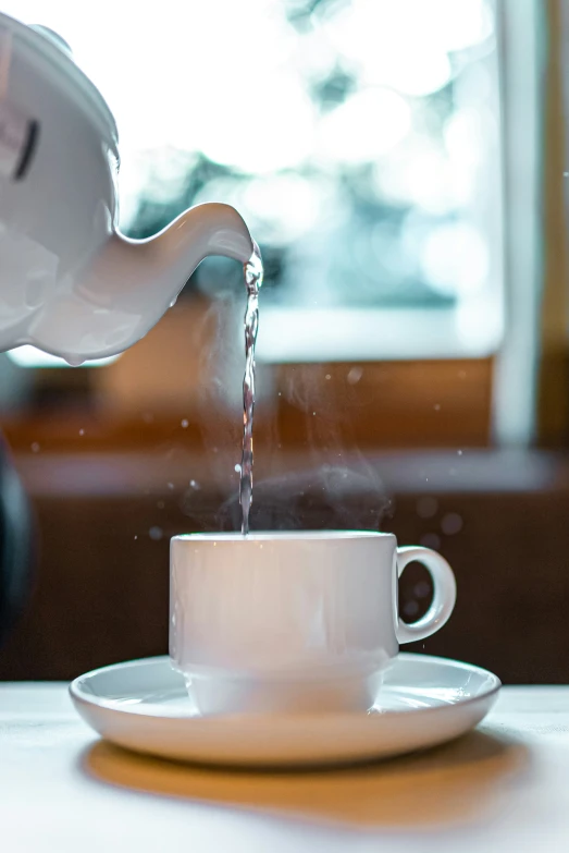 a person pouring water into a white coffee cup