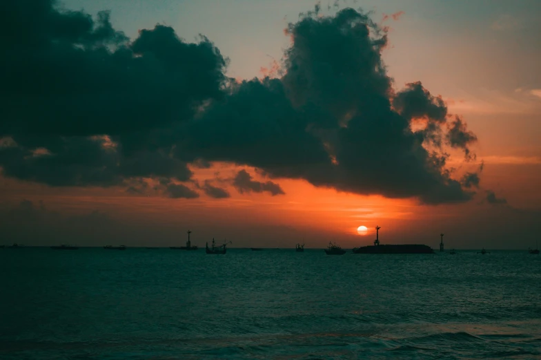 the sun rises behind clouds over ships off shore